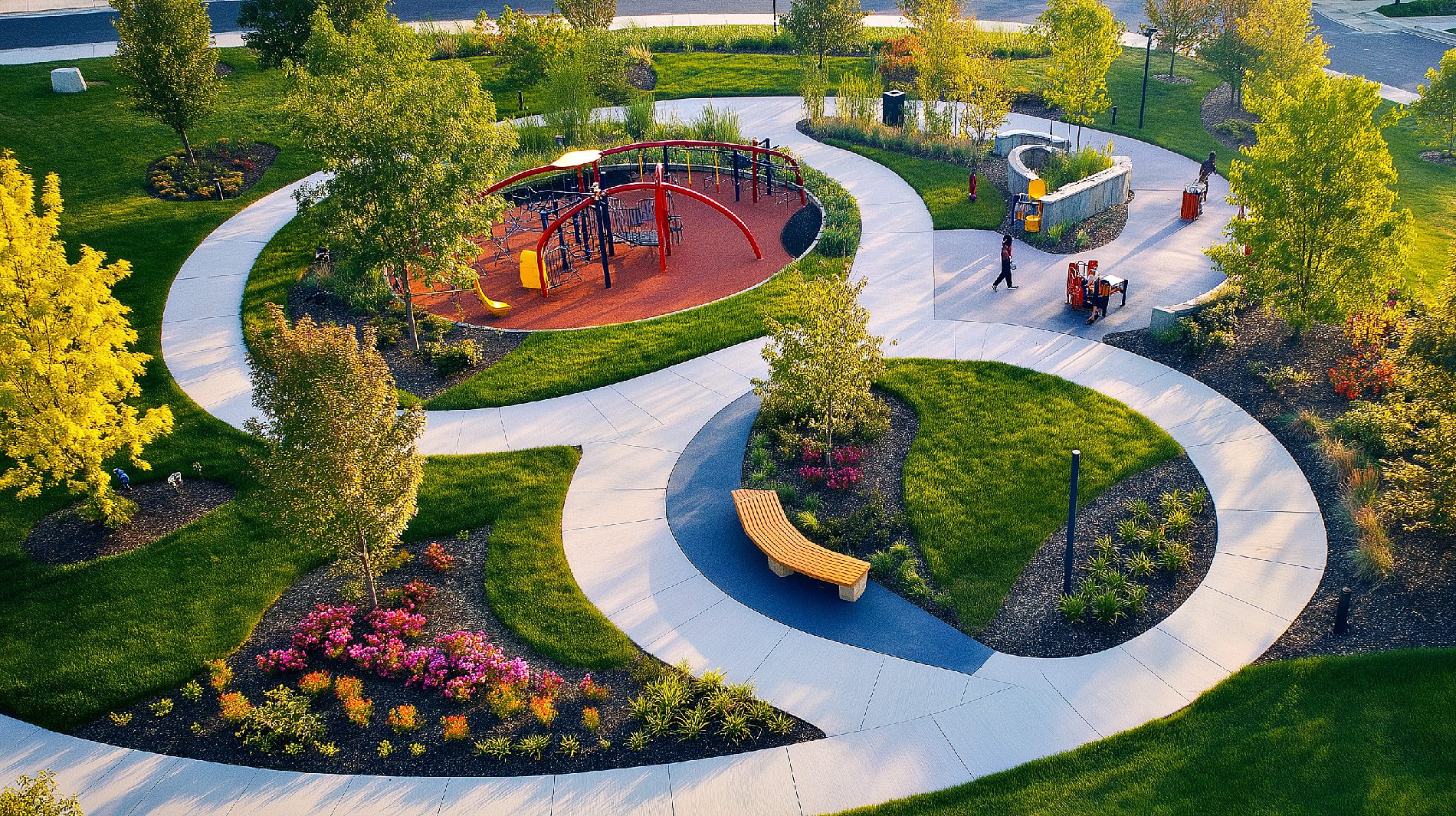 Luftaufnahme eines Parks mit zwei sich überschneidenden kreisförmigen Wegen, die Spielplatz und Picknickbereich verbinden.