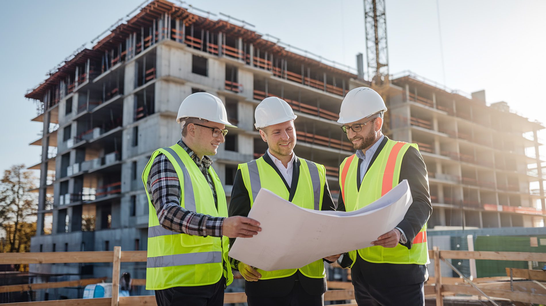 Architekt bespricht mit Bauträger und Vermesser Baupläne auf einer Baustelle im Morgenlicht
